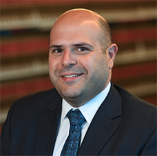 Richad Murdocco in a suit in front of shelves of books